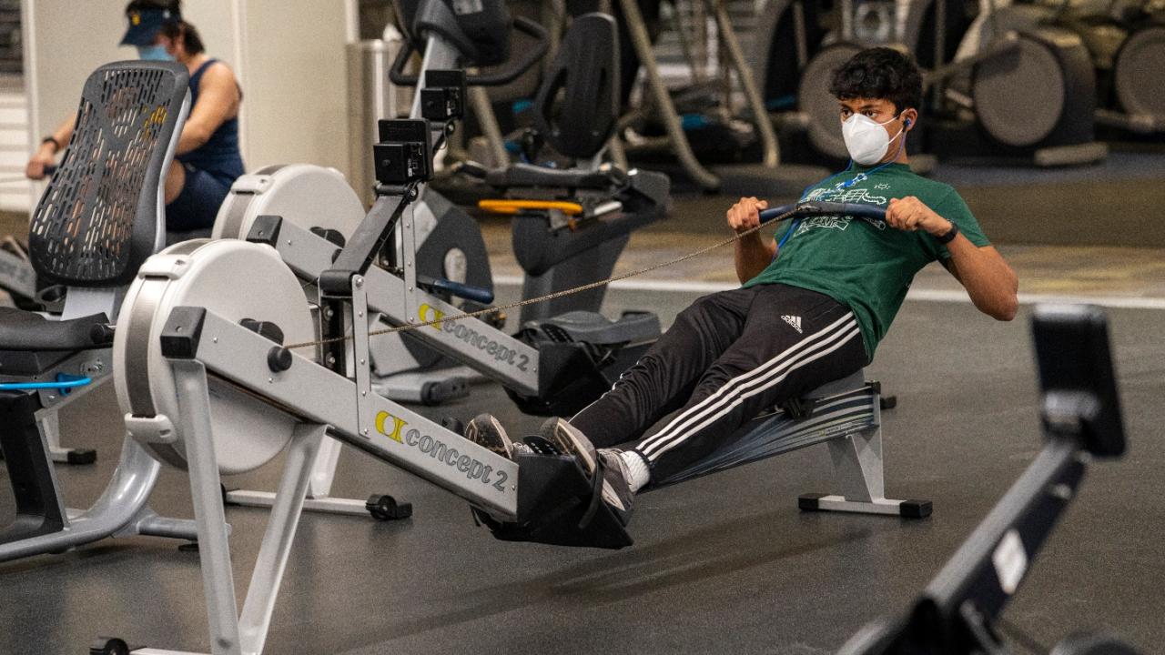 A student, wearing a mask, uses the rowing machine at the ARC