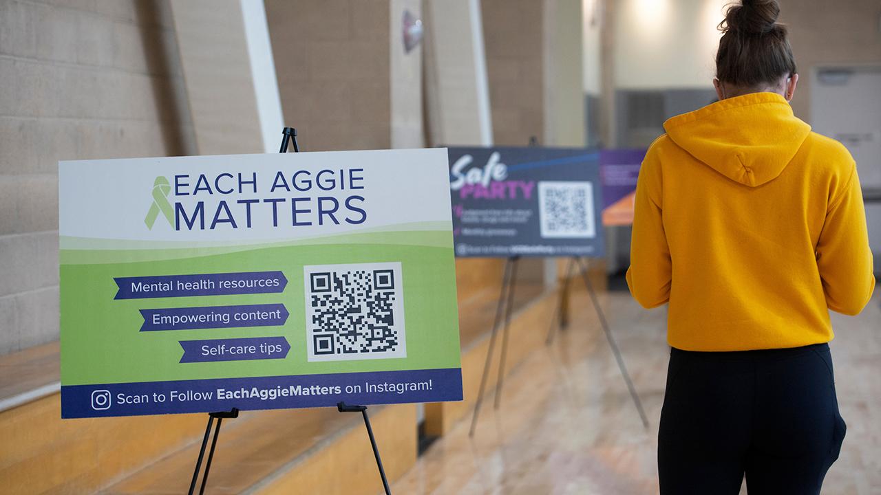 Student standing in line at ARC Pavilion by Each Aggie Matters sign