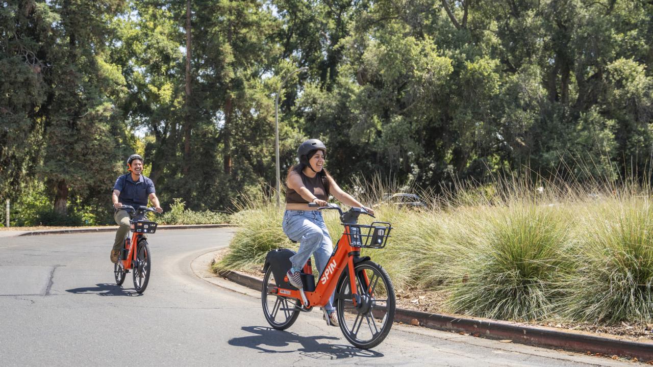 Two students ride on Spin bikes across campus