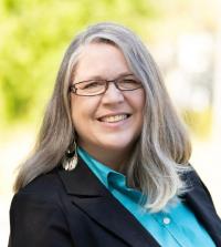 This is a image of Tiffani Francis, smiling with glasses, and trees in the background.
