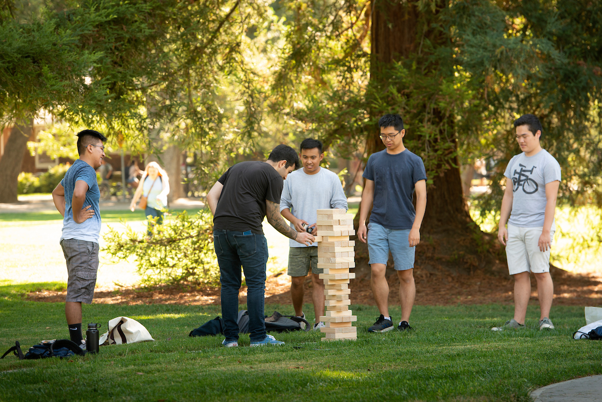 A group of friends play giant Jenga on the grass in the Quad