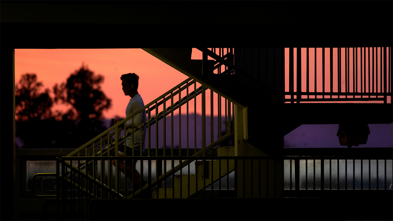 A student descends the stairs in a campus parking structure at sunset