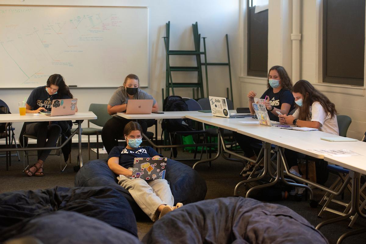 five members of the softball team study at tables and beanbags