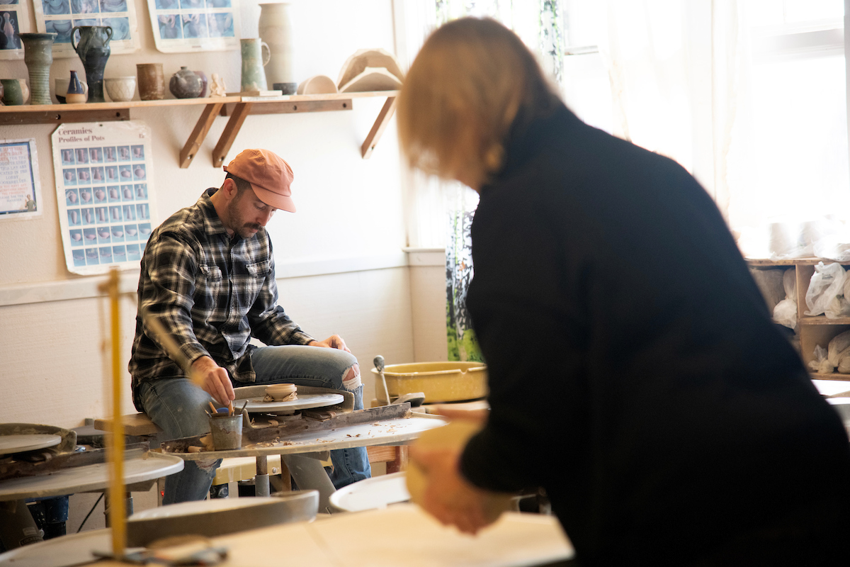 A community member works on a ceramic bowl on a pottery wheel in the Craft Center