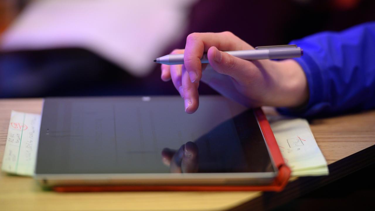 A student's hand hovers over a tablet device.