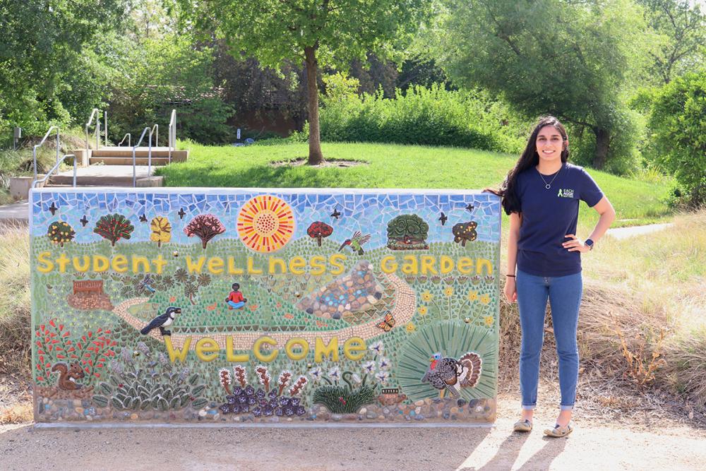 Roshni Desai standing by the Student Wellness Garden welcome sign
