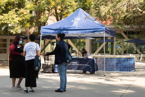 three people stand in front of a public health ambassador tent