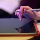 A student's hand hovers over a tablet device.