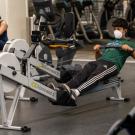 A student, wearing a mask, uses the rowing machine at the ARC
