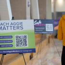 Student standing in line at ARC Pavilion by Each Aggie Matters sign